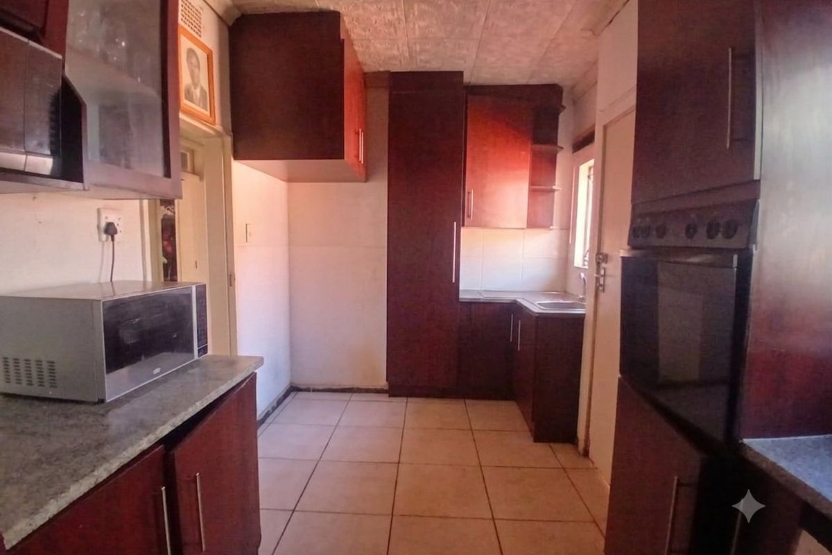 A dated kitchen featuring dark wood-look cabinetry, laminate countertops, built-in oven, and tiled flooring, offering potential for a modern renovation.