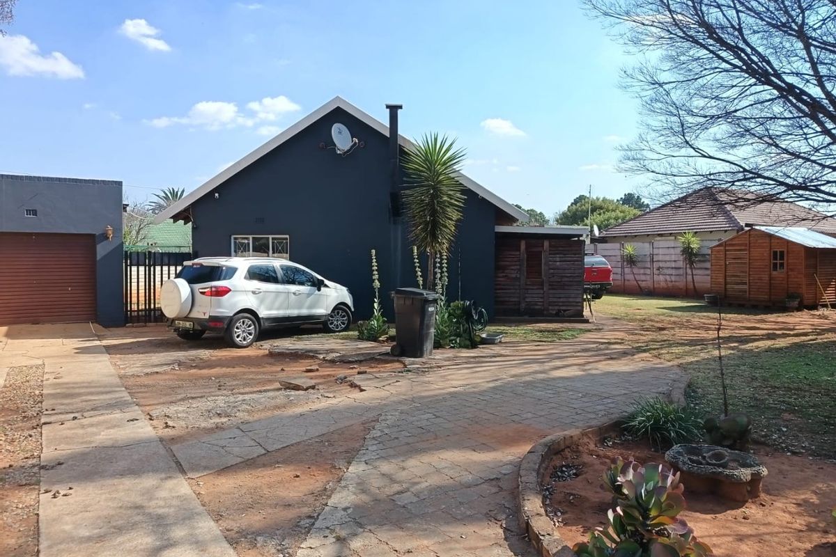Rear view of the property featuring a paved driveway, detached garage, and timber shed set within a large garden area.