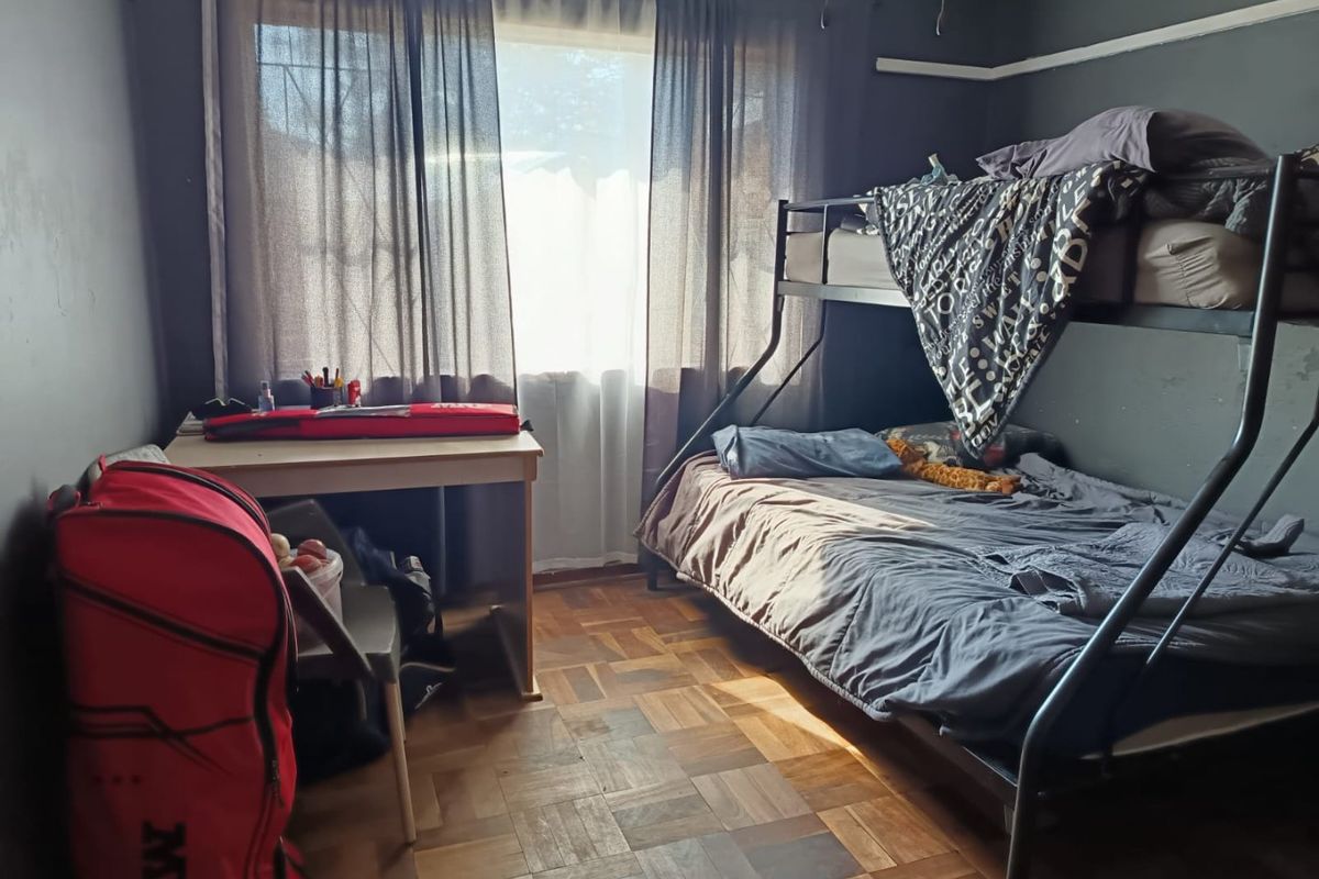 A bedroom featuring parquet flooring and dark-painted walls, offering a functional space with natural light from the window.
