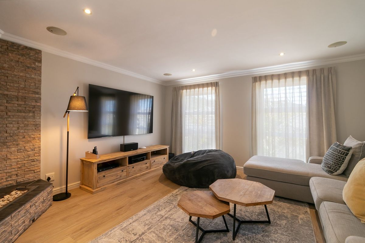 A well-maintained living room featuring a stone feature wall, recessed lighting, ceiling speakers, and laminate flooring, creating a comfortable and modern atmosphere.