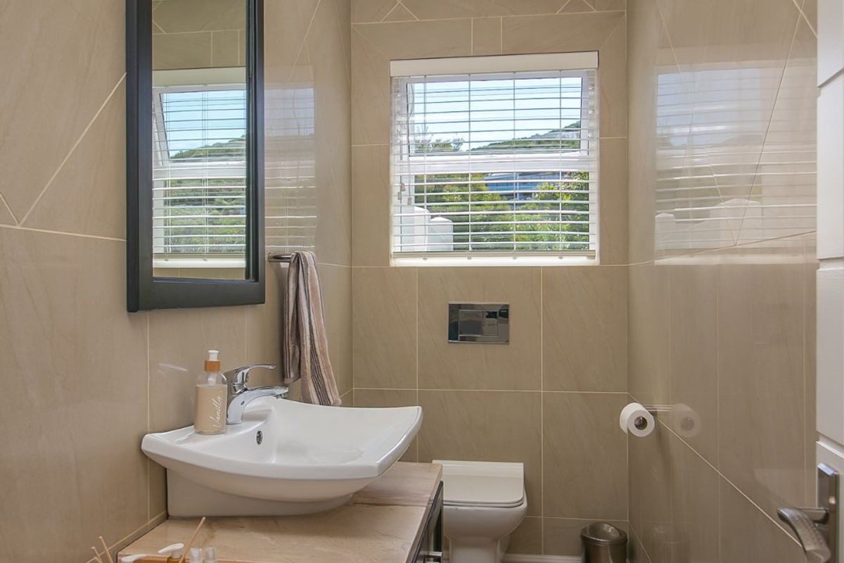 A modern guest bathroom featuring floor-to-ceiling beige tiling, a wall-mounted toilet with a concealed cistern, and a sleek vanity unit with a ceramic basin.