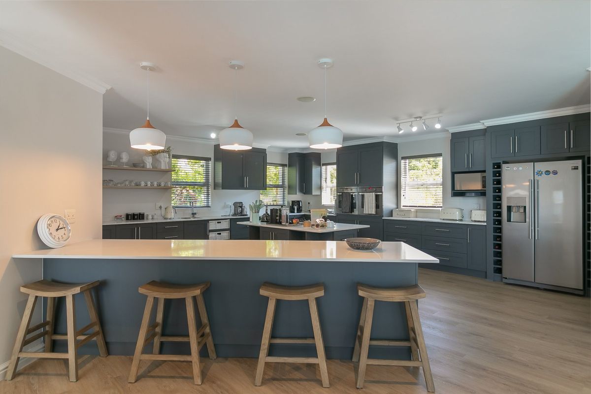 Modern, spacious kitchen featuring dark cabinetry, a large central island with quartz countertops, integrated appliances, and stylish pendant lighting.