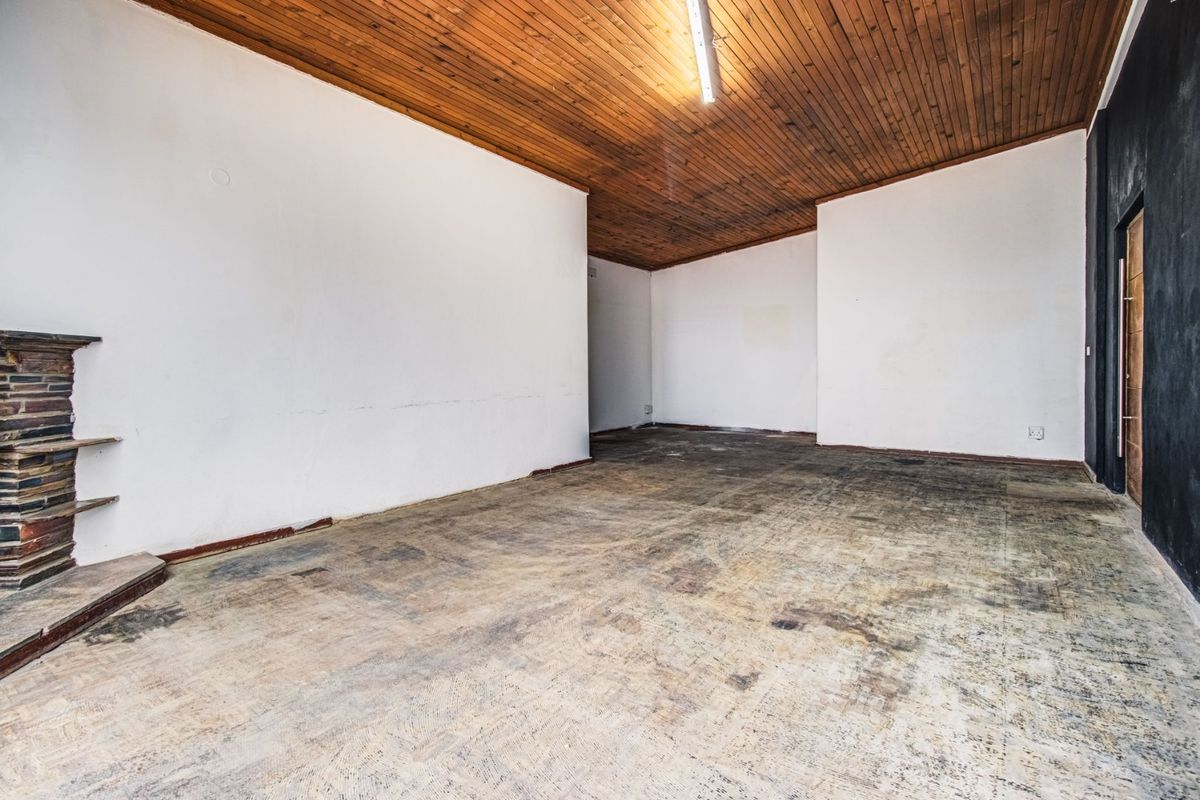 An empty commercial space featuring a stone fireplace, timber-clad ceiling, and worn flooring, offering a blank canvas for renovation and interior design updates.