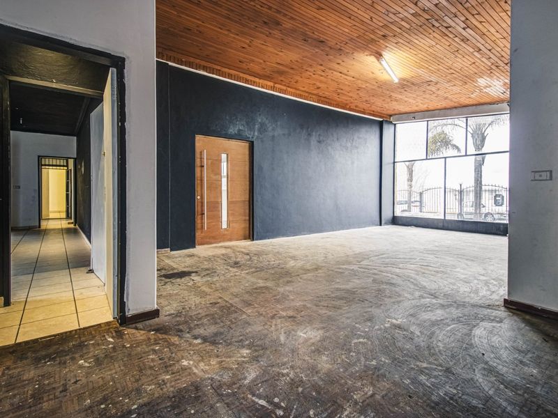 Spacious open-plan commercial area featuring a timber ceiling, large storefront windows, and direct access to a tiled hallway.