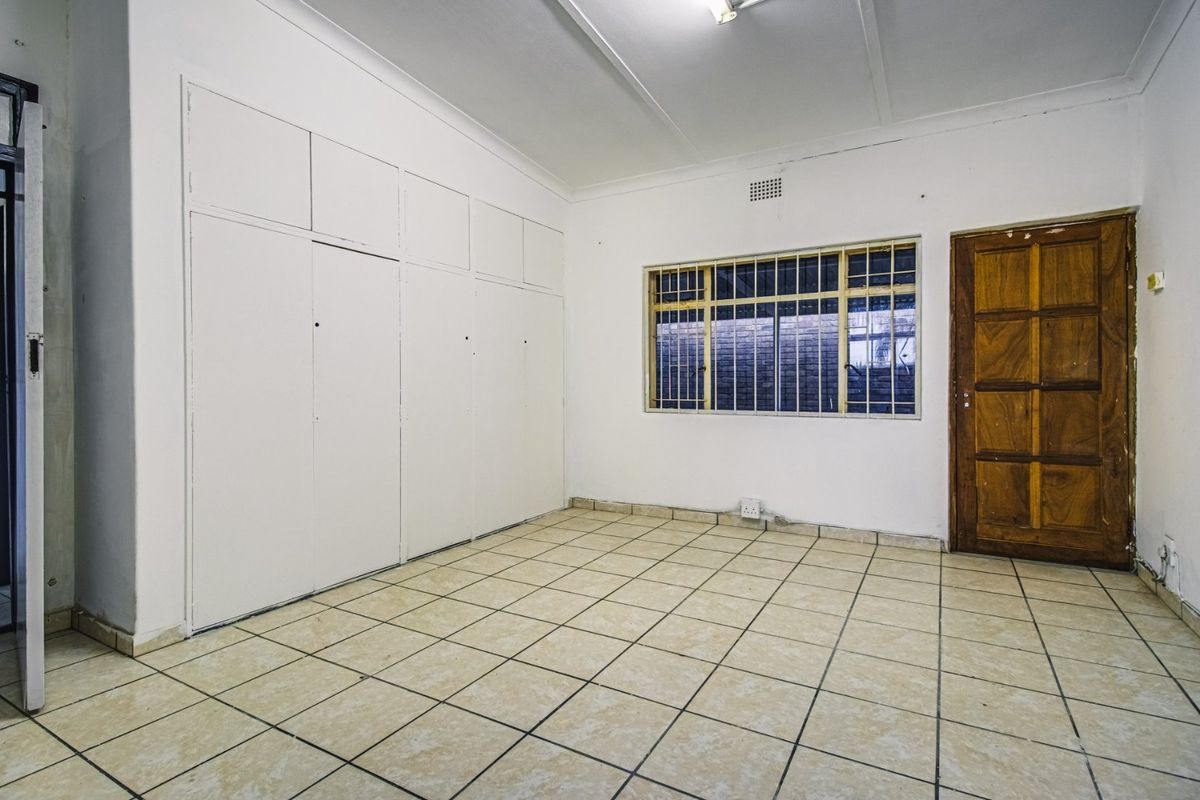 An empty bedroom featuring tiled flooring, built-in cupboards, and a wooden door, providing a blank canvas for renovation or staging.