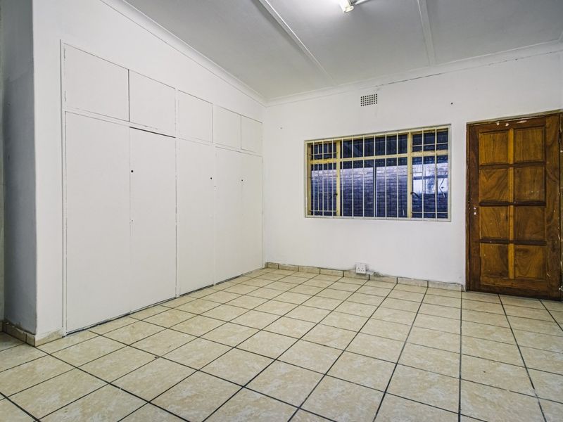 An empty bedroom featuring tiled flooring, built-in cupboards, and a wooden door, providing a blank canvas for renovation or staging.