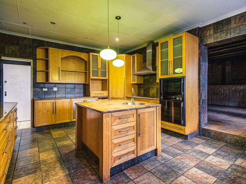 Spacious kitchen featuring wooden cabinetry, a central island with a sink, built-in oven, and durable tiled flooring throughout.