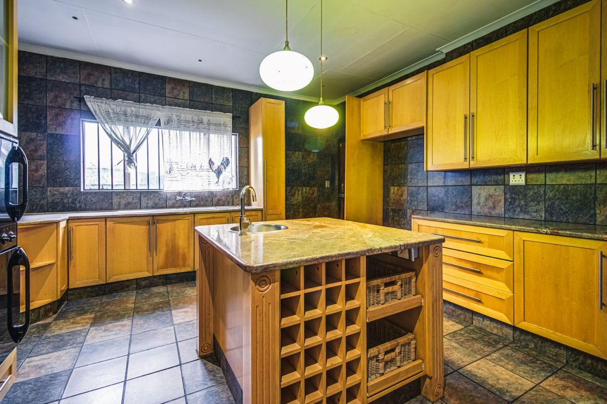 Spacious kitchen featuring wooden cabinetry, a central island with a built-in wine rack, stone countertops, and dark tiled finishes.
