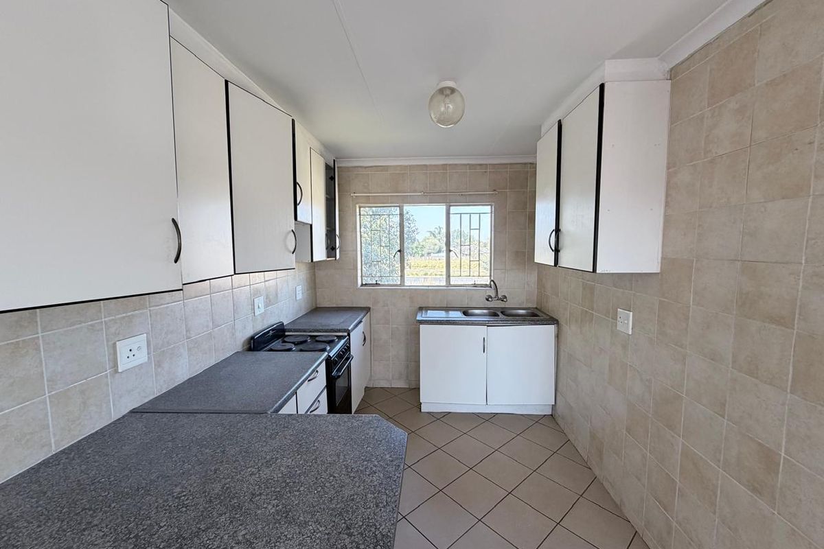 A functional, galley-style kitchen featuring built-in cabinetry, laminate countertops, a stainless steel sink, and a built-in stove with tiled walls and flooring.