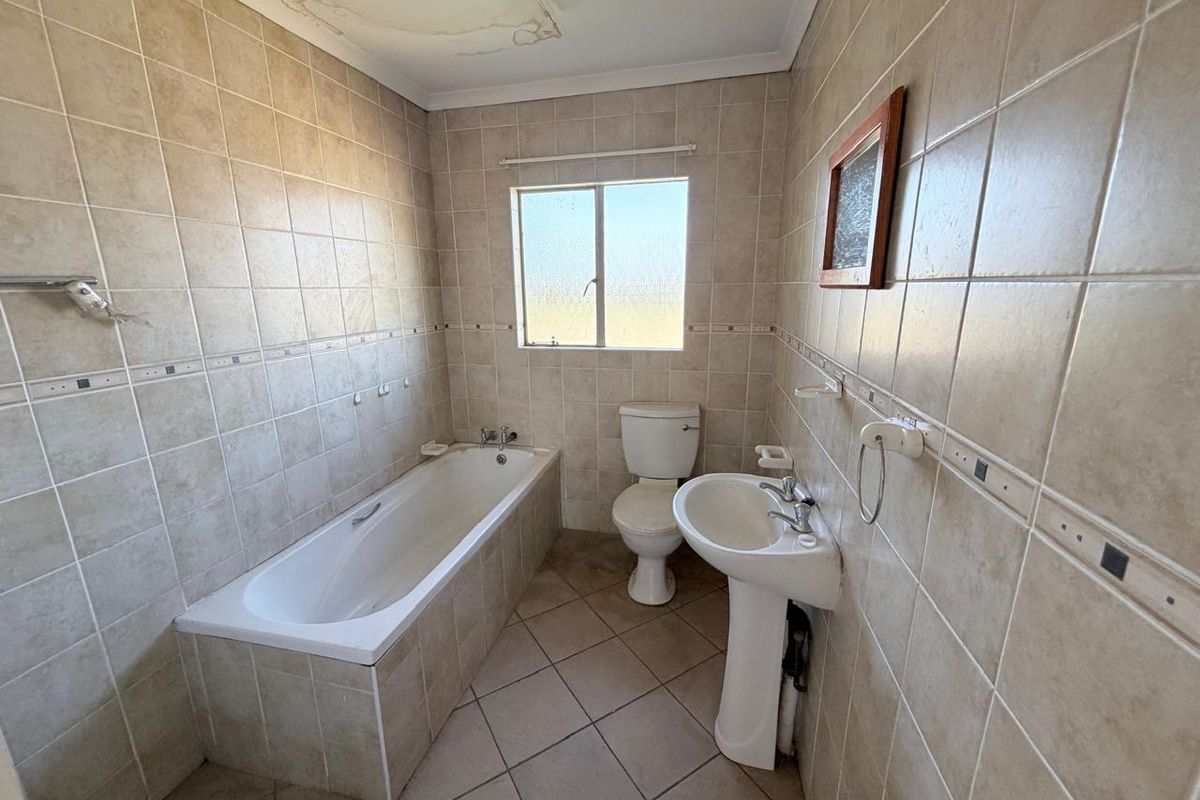 A functional bathroom featuring tiled walls and flooring, a pedestal basin, a built-in bathtub, and a toilet, requiring minor cosmetic updates.