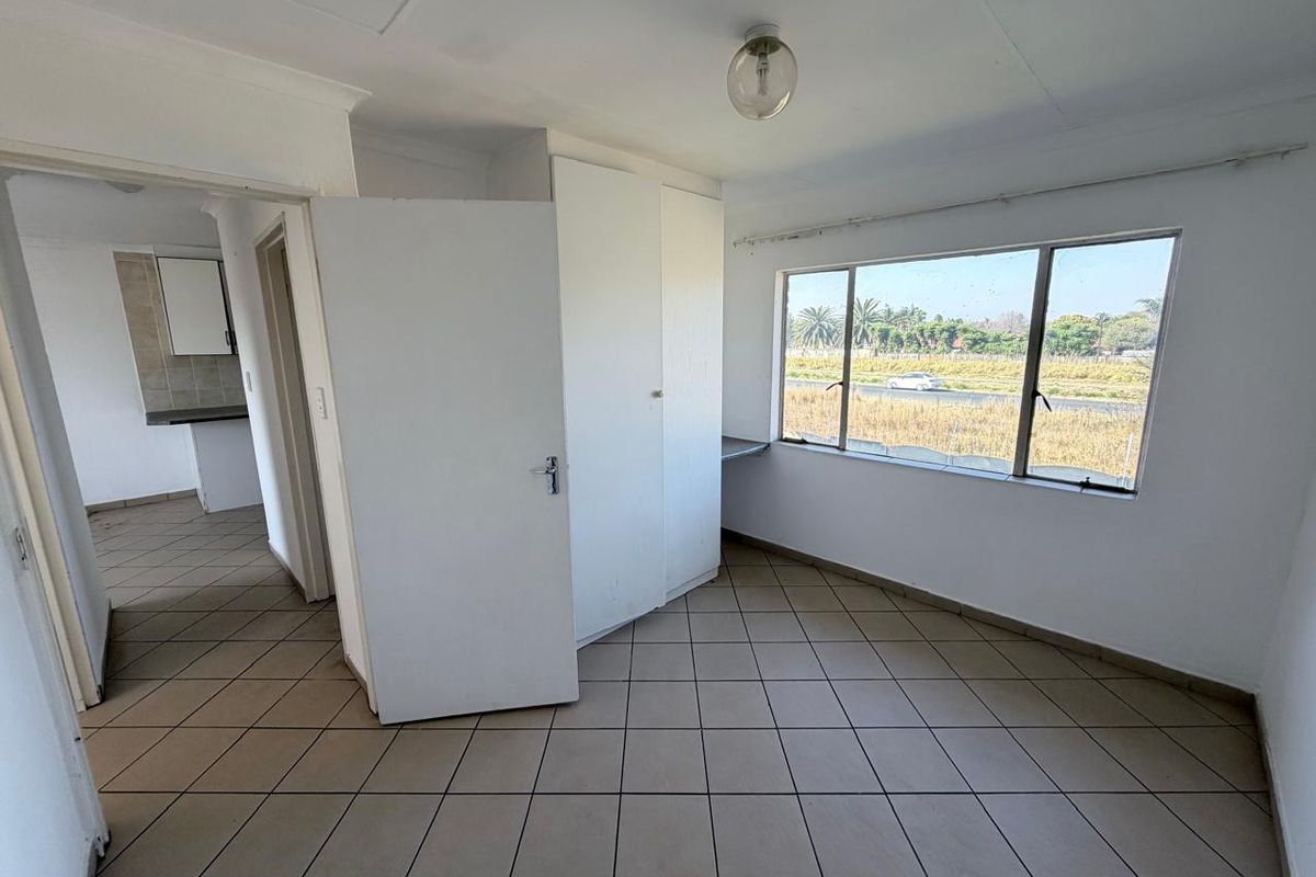 An empty bedroom featuring tiled flooring, built-in cupboards, and a large window with views of the surrounding area.