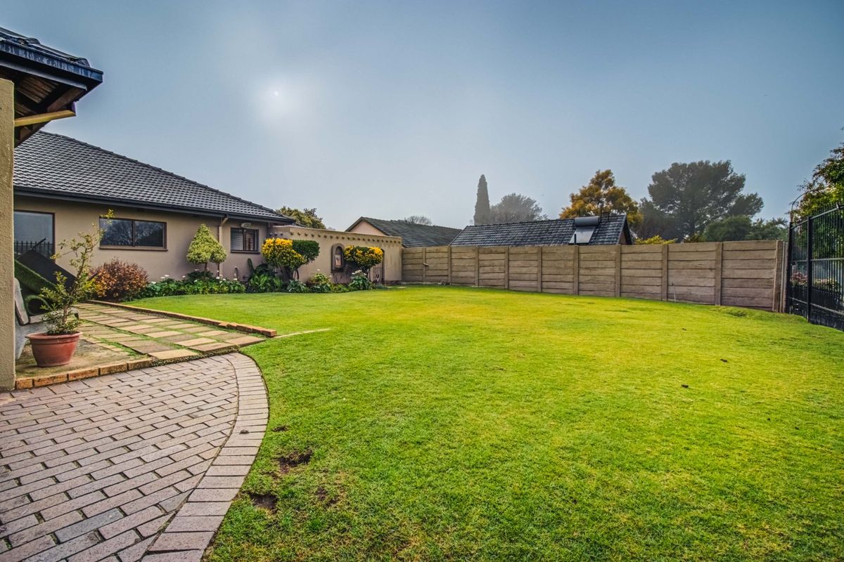 A well-maintained rear garden featuring a paved patio area, lush lawn, and secure precast concrete boundary walling.