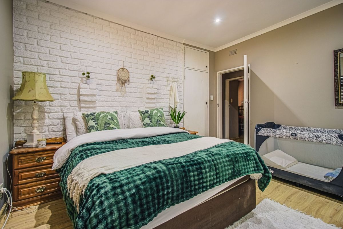 A well-maintained bedroom featuring a textured white exposed brick feature wall, laminate flooring, and built-in storage cabinetry.