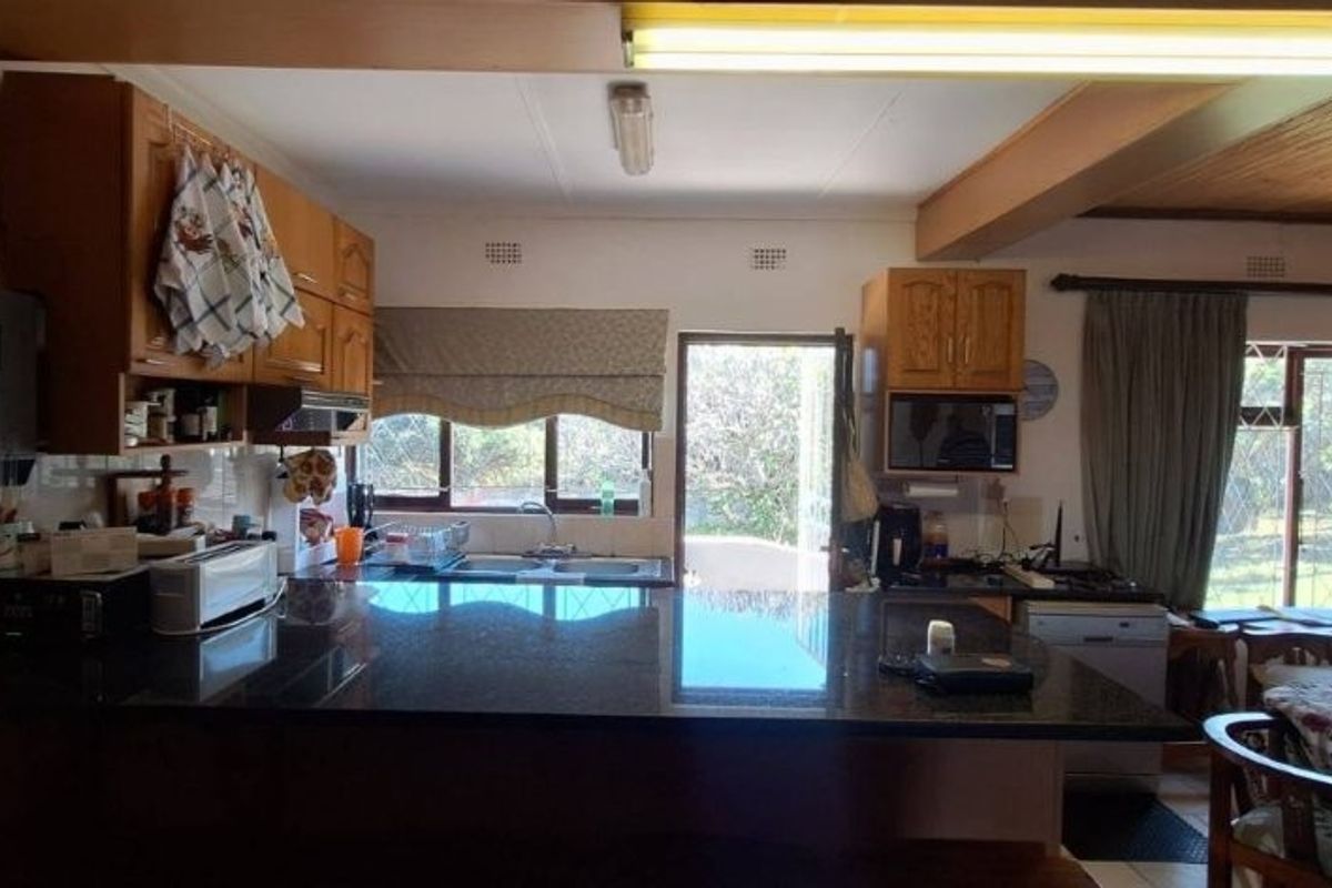 A functional kitchen featuring granite countertops, ample wooden cabinetry, and a timber ceiling, with direct access to the outdoor area.