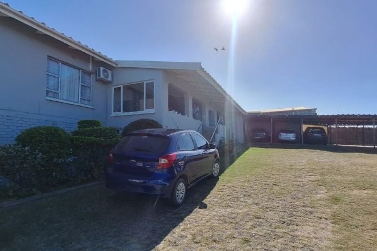Rear exterior view of the townhouse featuring a lawn area, carport structure, and external air conditioning unit.