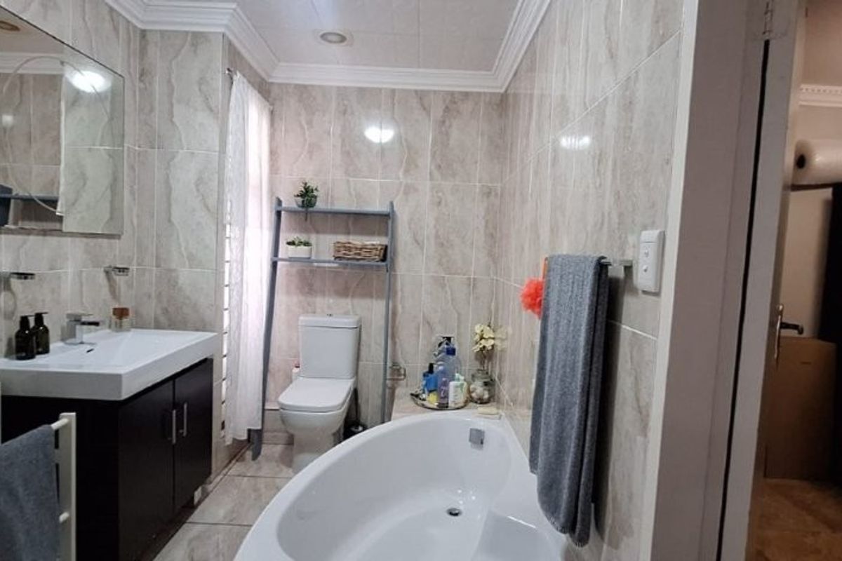 A well-maintained bathroom featuring a modern vanity, bathtub, toilet, and floor-to-ceiling tiled walls with neutral finishes.