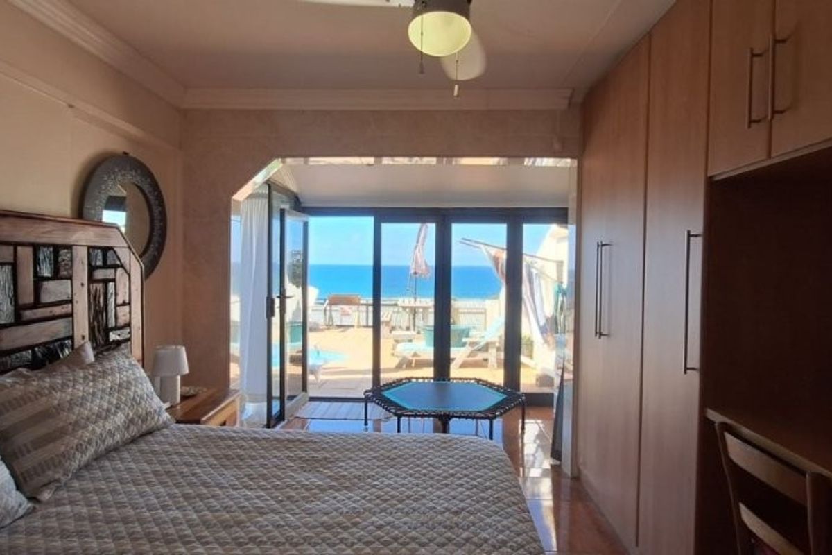 Spacious bedroom featuring built-in cupboards, ceiling fan, and large sliding glass doors opening to a patio with ocean views.