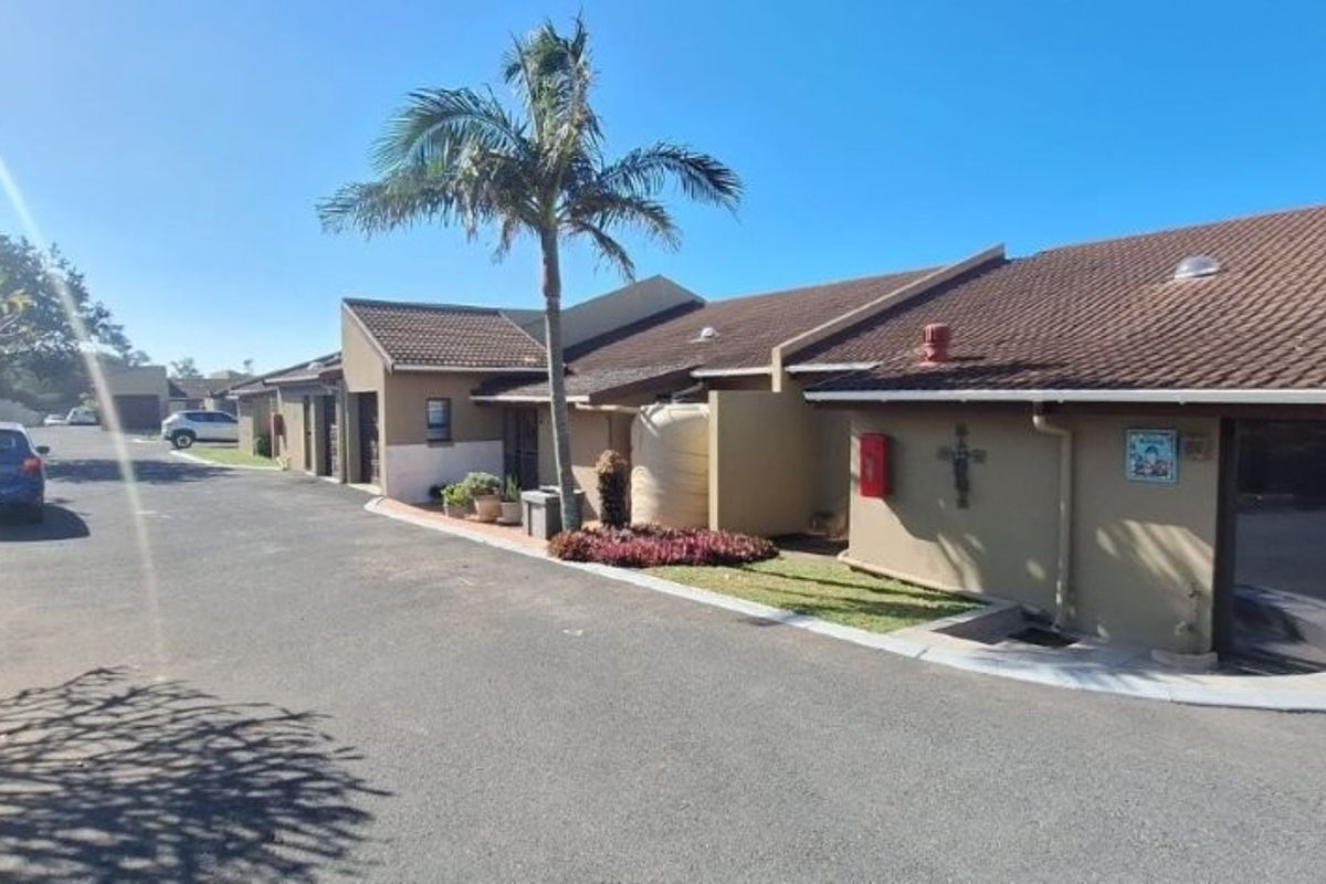 Front exterior view of the townhouse complex featuring a paved driveway, tiled roof structure, and established garden area.