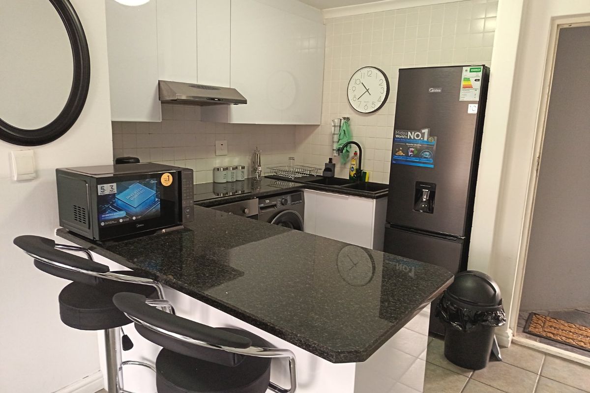A compact, modern kitchen featuring white cabinetry, dark granite countertops, a tiled backsplash, and integrated appliances, offering a functional and clean workspace.