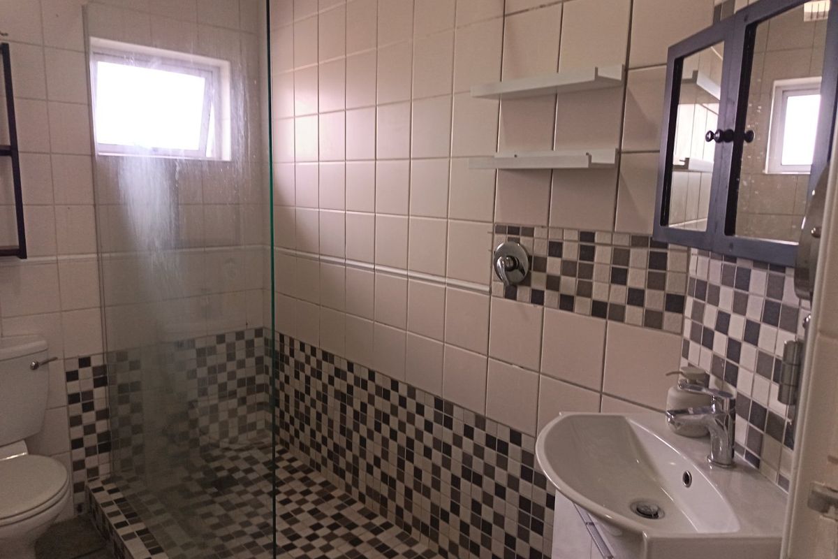 A functional bathroom featuring a walk-in shower with a glass screen, vanity basin, and a toilet, finished with a checkered tile accent.