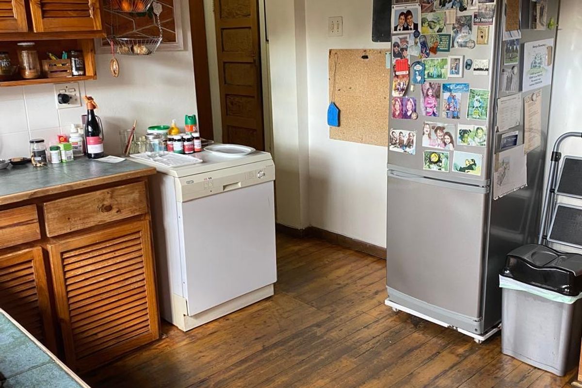 A functional kitchen featuring wooden cabinetry, laminate countertops, and original hardwood flooring, leading through an archway to an adjacent room.