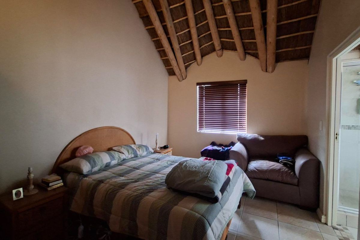 A bedroom featuring a high vaulted ceiling with exposed timber rafters, thatched roofing, tiled floors, and an adjoining en-suite bathroom.