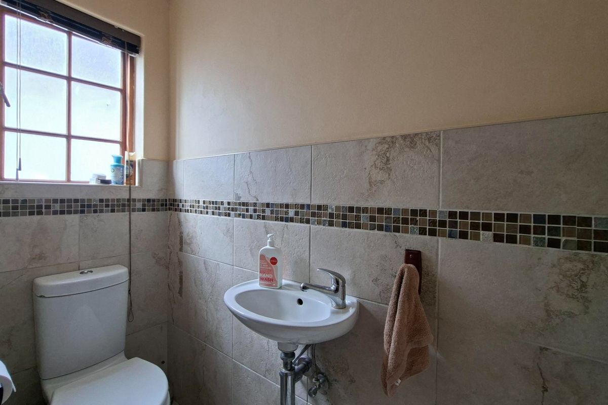 A compact guest bathroom featuring neutral ceramic wall tiles with a decorative mosaic border, a pedestal basin, and a dual flush toilet.