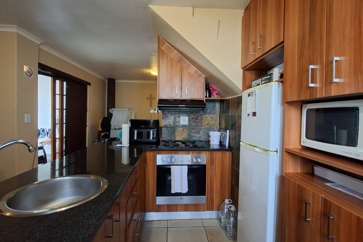 A functional kitchen featuring wood-finish cabinetry, granite countertops, built-in oven and hob, and a tiled splashback, offering a practical layout for daily use.