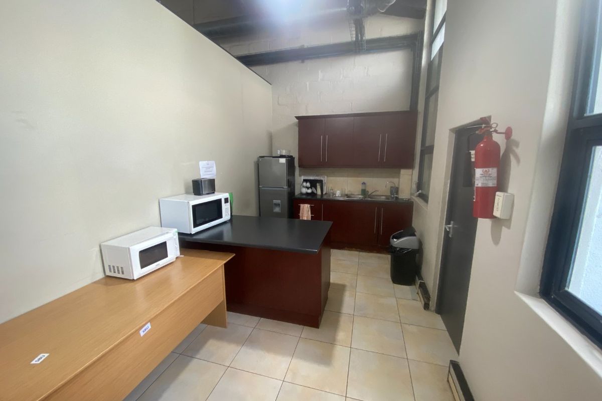 A functional commercial kitchenette featuring dark wood cabinetry, a sink, tiled flooring, and exposed industrial-style ceiling ducting.