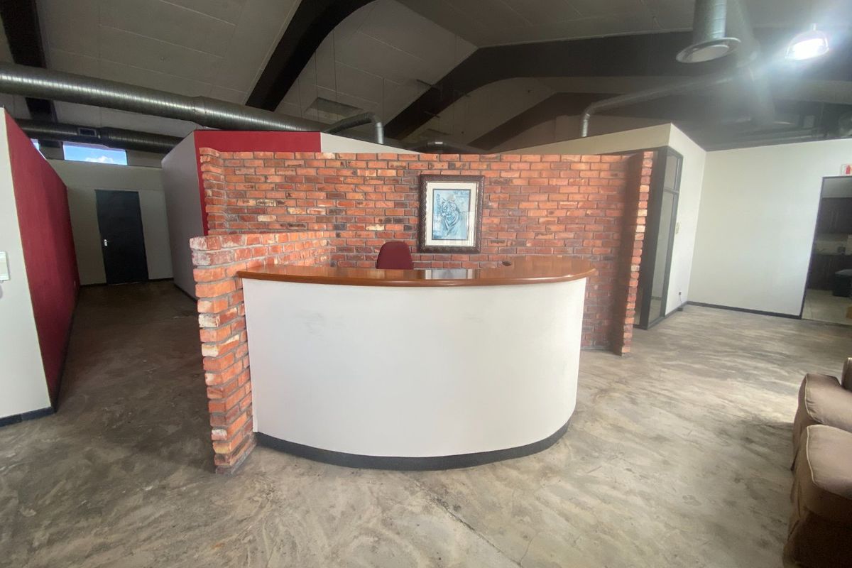 Commercial entrance area featuring a built-in reception desk, exposed brick wall, and industrial-style exposed ducting with concrete flooring.