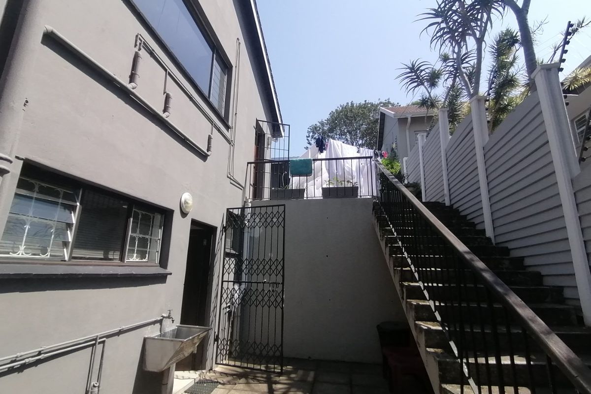 Rear exterior courtyard featuring a paved area, external staircase with metal railing, security gate, and a wall-mounted utility sink.