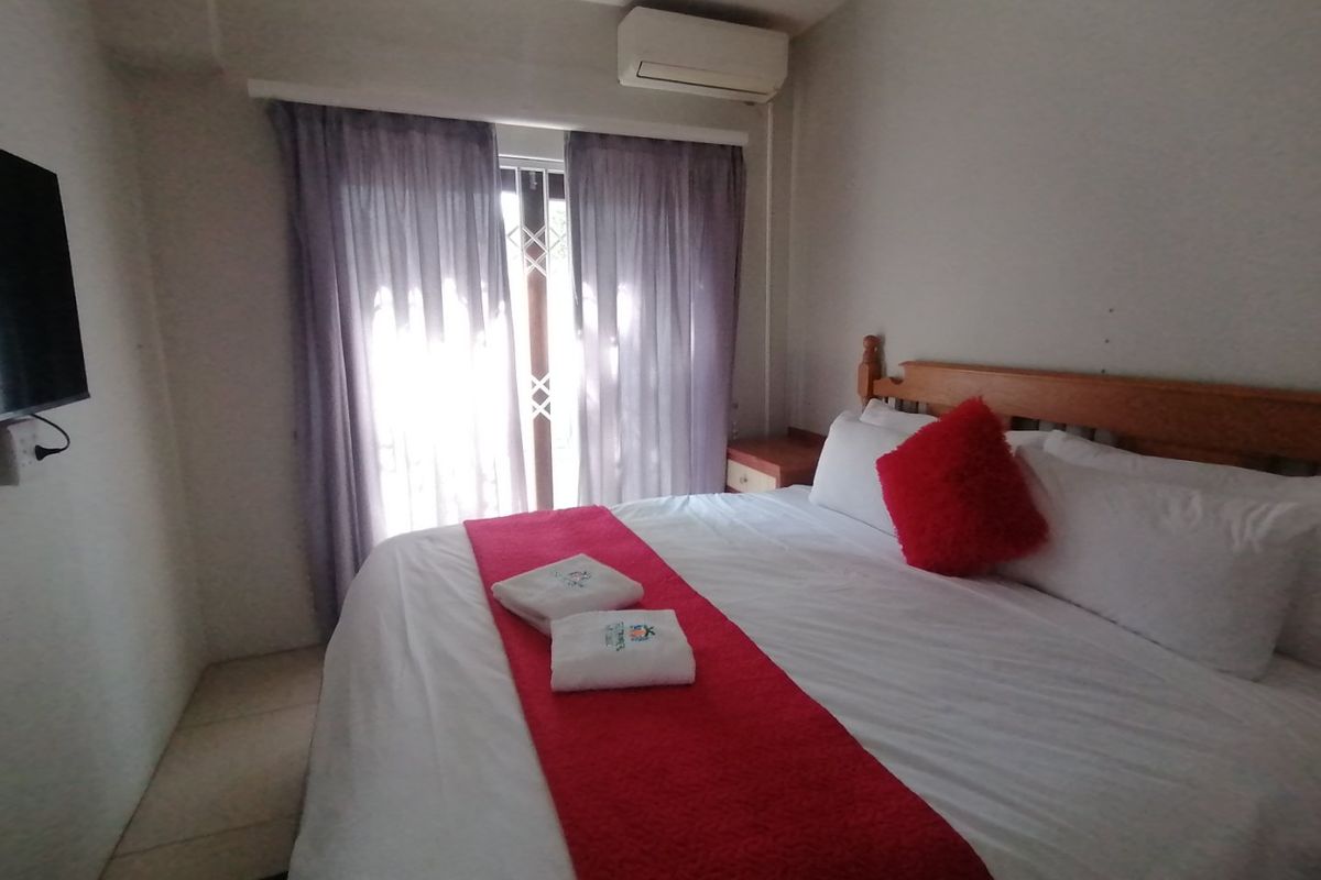 A functional bedroom featuring a wall-mounted air conditioning unit and a sliding glass door with an integrated security gate.
