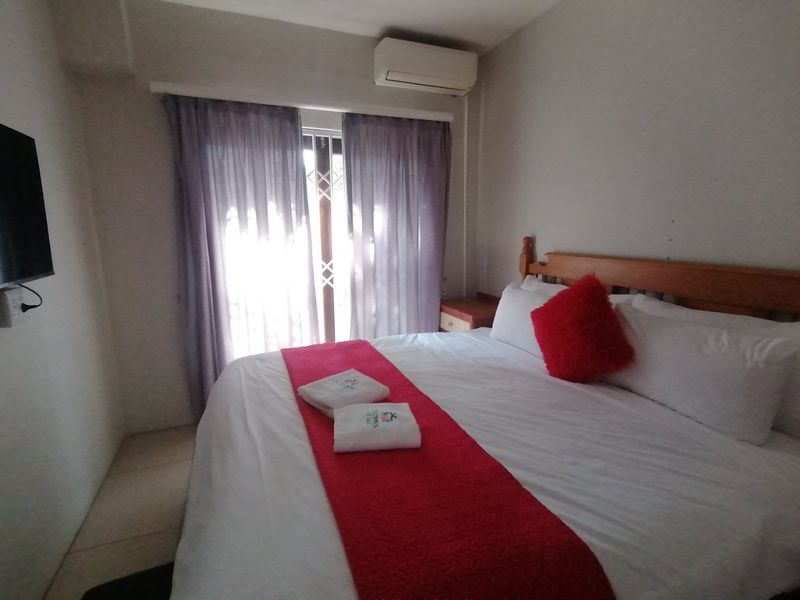 A functional bedroom featuring a wall-mounted air conditioning unit and a sliding glass door with an integrated security gate.