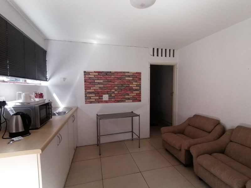 Open plan living area featuring a compact kitchenette with laminate countertops, stainless steel sink, tiled flooring, and neutral wall finishes.