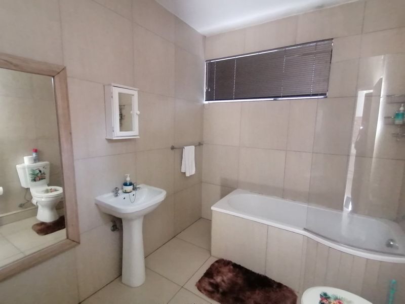 A functional bathroom featuring a pedestal basin, bathtub with a glass shower screen, and neutral wall tiling throughout.