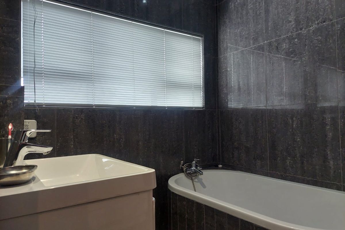 Modern bathroom featuring dark stone-look wall tiles, a built-in bathtub, and a contemporary vanity basin with a mixer tap.