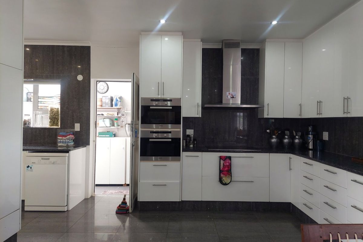 Modern kitchen featuring high-gloss white cabinetry, dark stone countertops, built-in stainless steel appliances, and tiled flooring, with an adjacent scullery area.