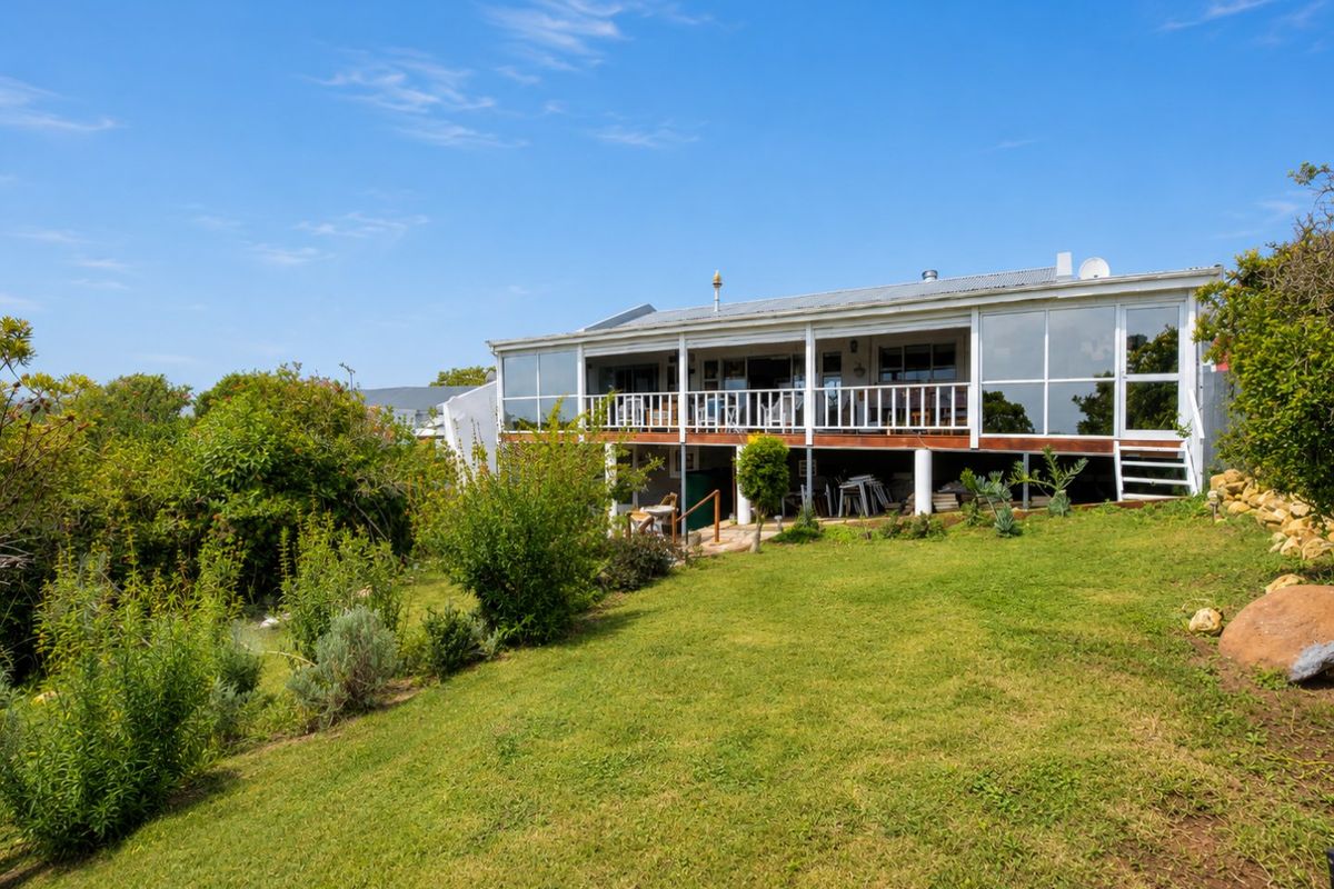 Rear view of the property featuring an elevated wooden deck with white balustrades, large glass windows, and a spacious landscaped garden.