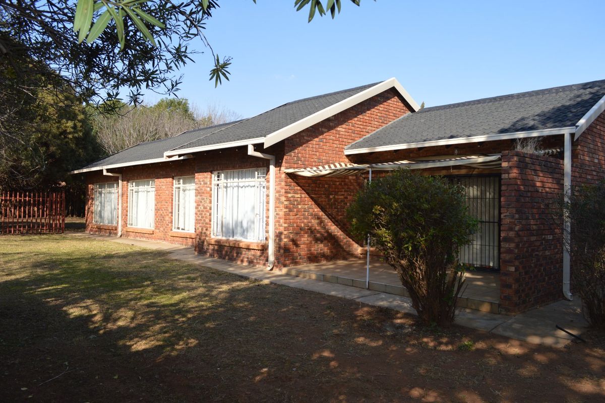 Rear view of a face brick house featuring a paved patio area, retractable awning, and secure entrance, set within a garden space.