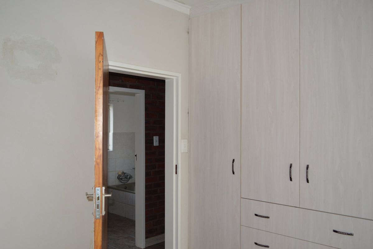 A bedroom interior featuring built-in cupboards and a view into an adjacent bathroom, showing minor wall surface damage.