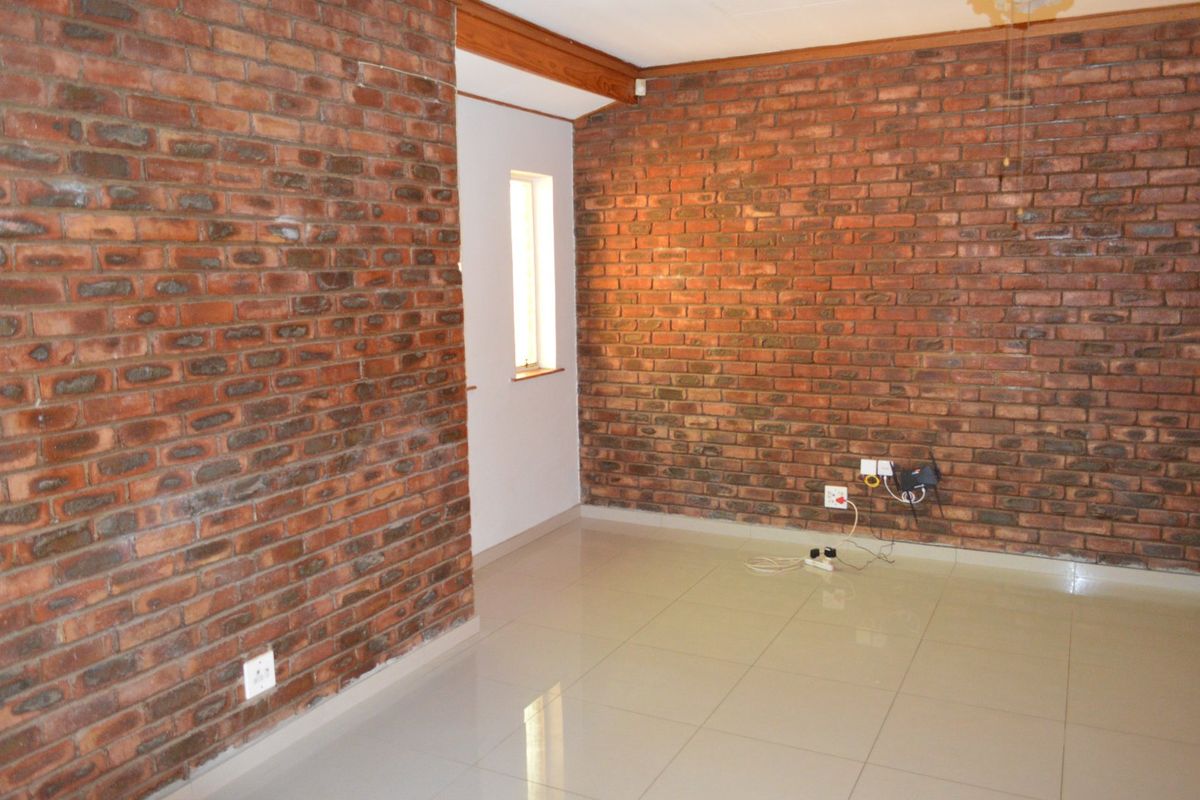 An empty living room featuring characterful exposed brick walls and neutral ceramic floor tiles, offering a blank canvas for interior design.