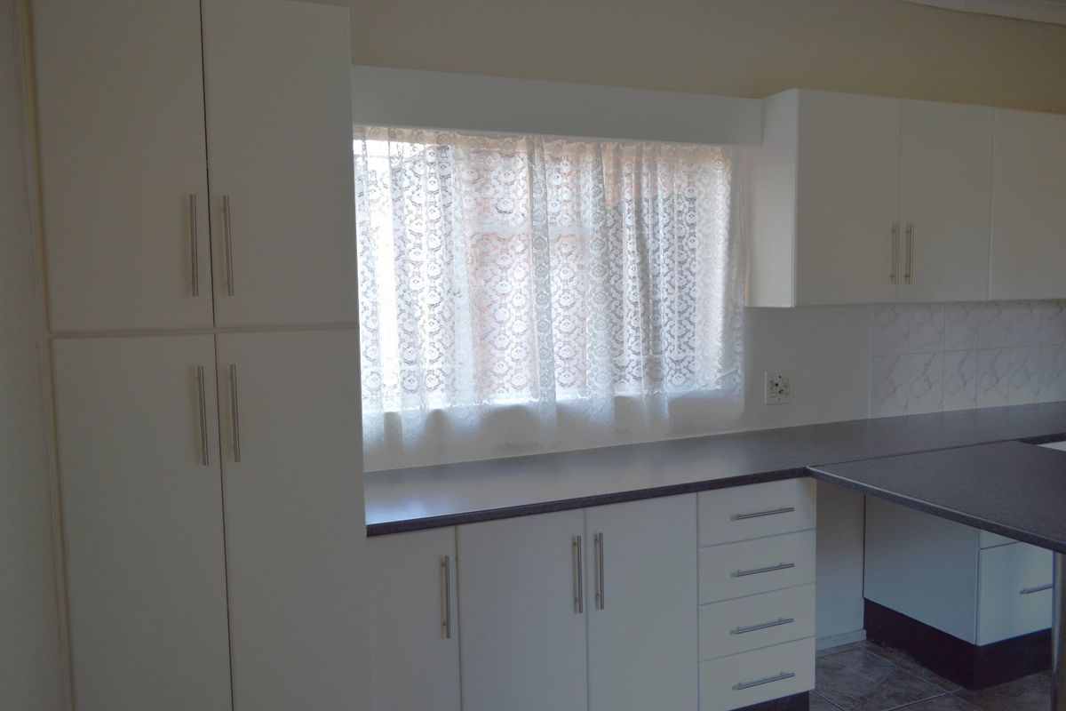 A clean, functional kitchen area featuring white built-in cabinetry, dark laminate countertops, and a tiled backsplash.