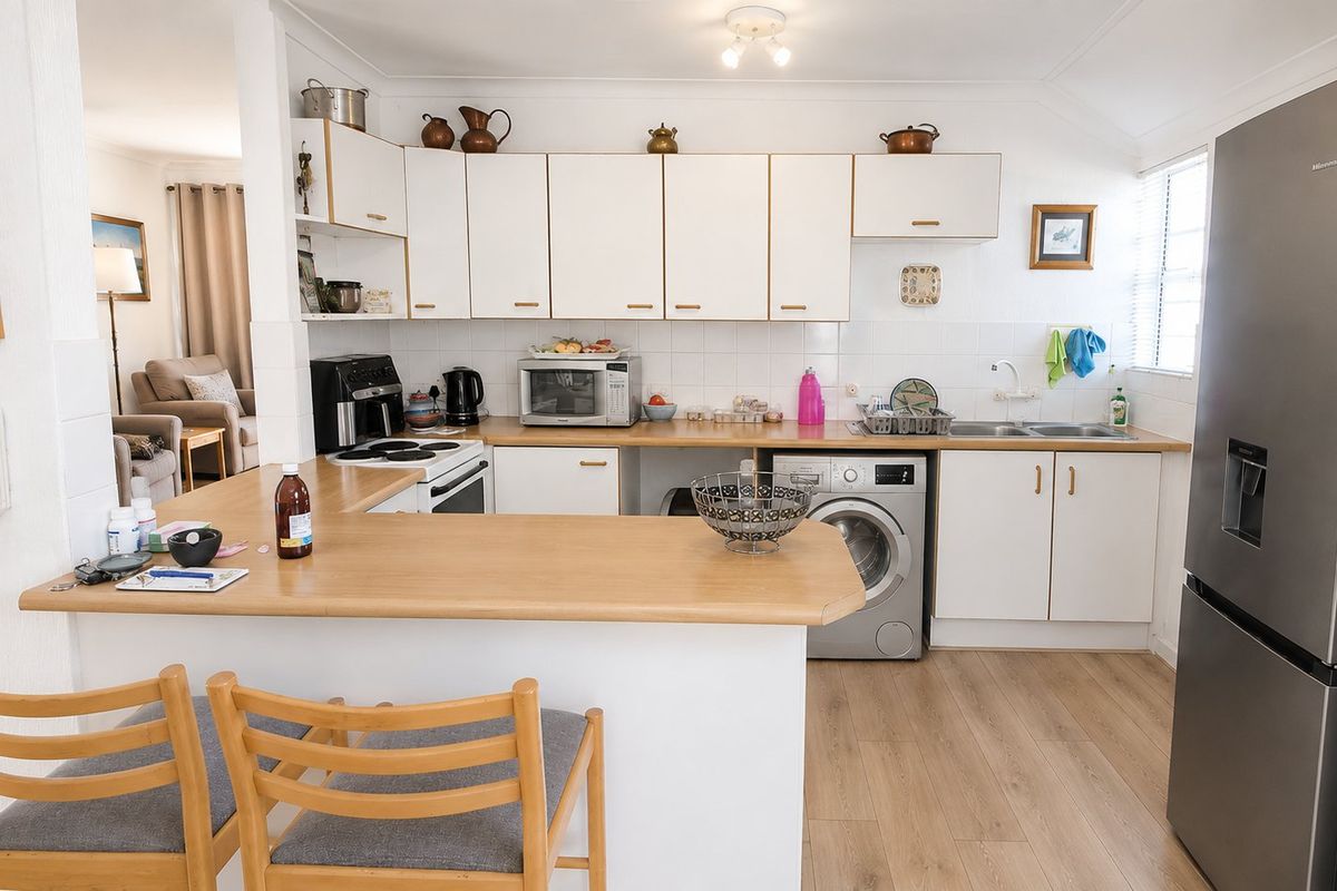 Functional kitchen featuring white cabinetry, laminate countertops, a breakfast bar, and integrated laundry facilities, opening into the adjacent living area.