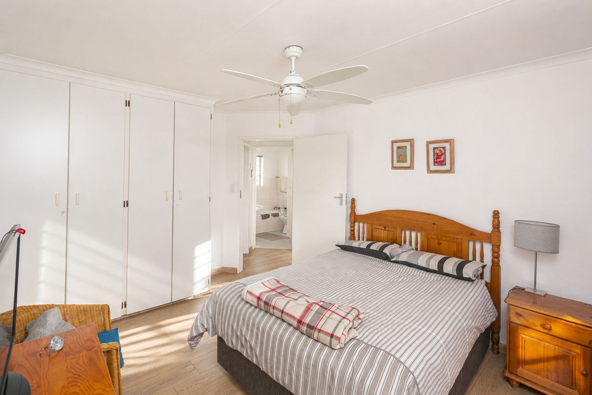 A well-lit bedroom featuring built-in cupboards, a ceiling fan, and laminate flooring, with an adjoining en-suite bathroom visible through the doorway.