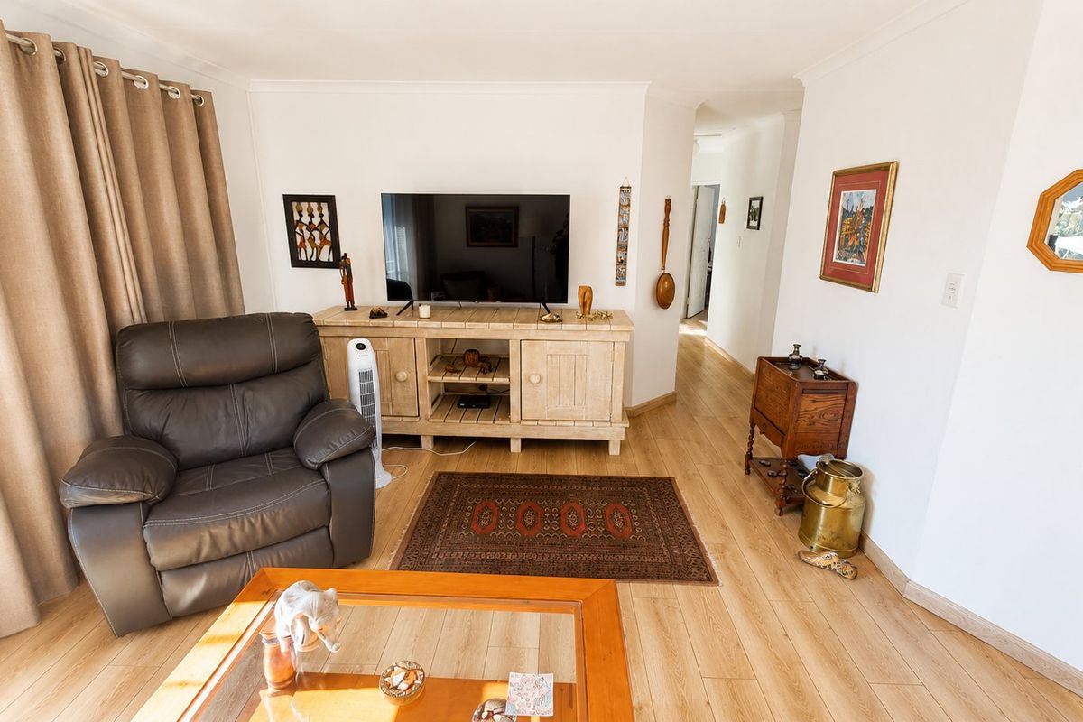 A well-maintained living room featuring light-toned laminate flooring, neutral walls, and classic cove cornicing, creating a bright and comfortable living space.