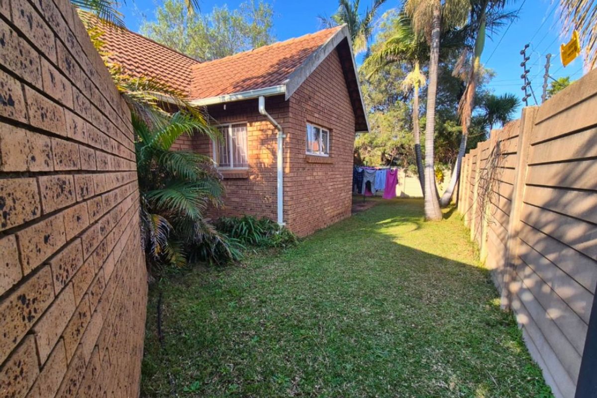 A view of the rear garden area featuring a brick exterior facade, tiled roof, and perimeter boundary walls.