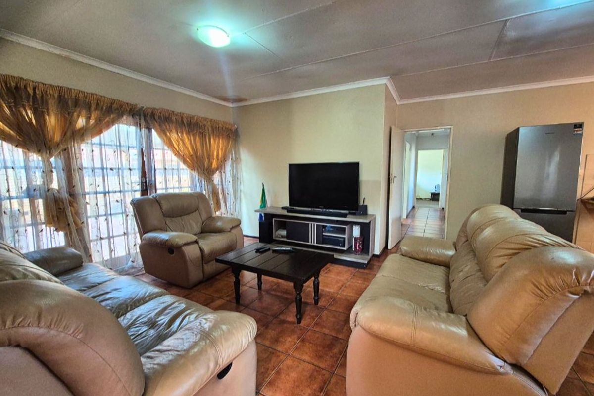 A living room featuring tiled flooring and a sliding glass door providing natural light, leading to an adjacent hallway.