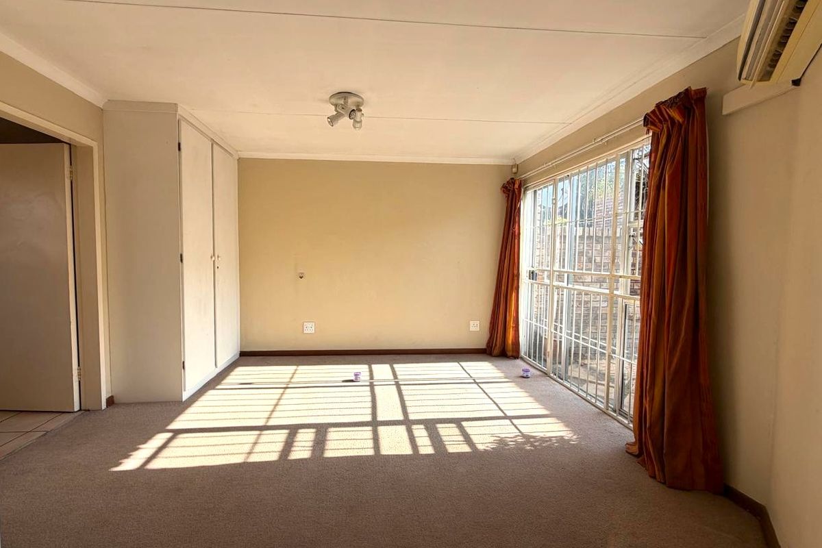 Spacious living room featuring neutral walls, built-in storage cupboards, an air conditioning unit, and large sliding glass doors with security bars.