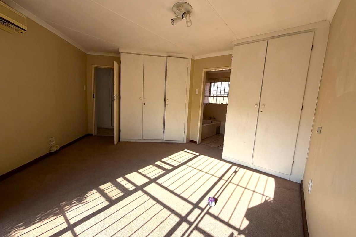 Spacious bedroom featuring built-in cupboards, carpeted flooring, and a wall-mounted air conditioning unit, offering a blank canvas for renovation.