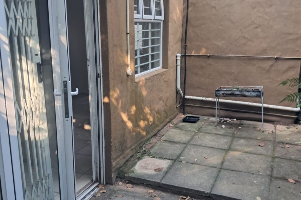 A small rear paved courtyard area featuring a sliding door entrance with security gate, external drainage, and wall-mounted lighting.